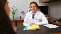 Male physician at desk, talking to patient.